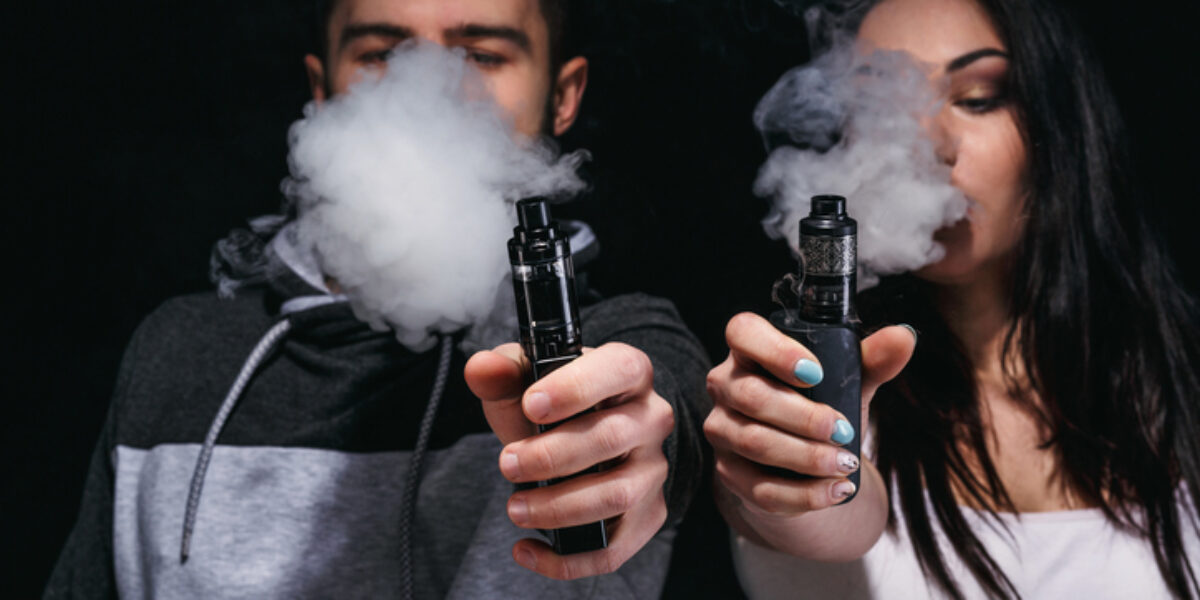 Couple vaping e-cigarette with smoke on black