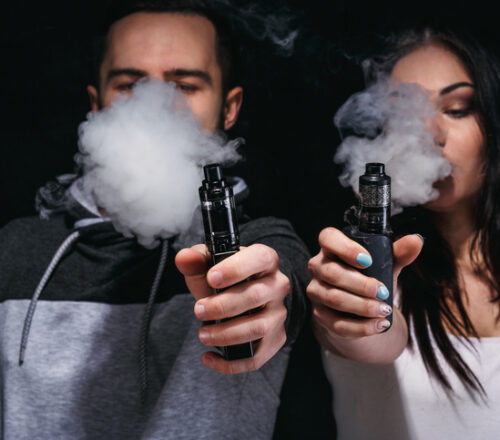 Couple vaping e-cigarette with smoke on black