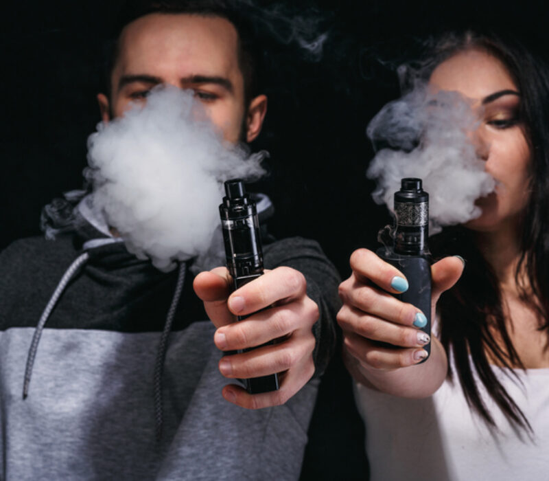 Couple vaping e-cigarette with smoke on black